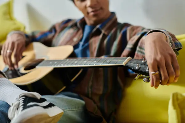 Young man serenades with acoustic guitar on cozy yellow couch. — Fotografia de Stock