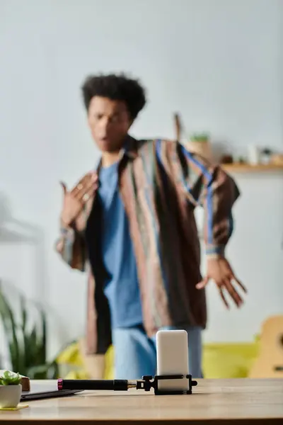 A young African American male blogger is standing in front of a table, talking on his phone camera. — Stock Photo
