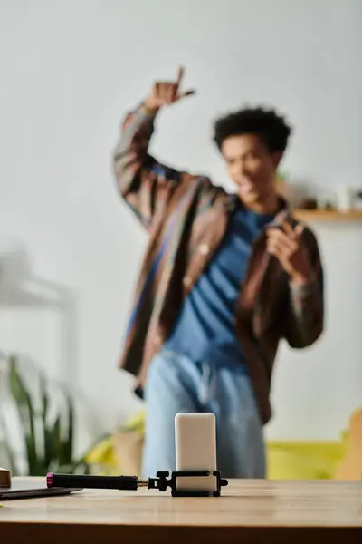 Young African American man stands on table, phone in hand, blogger vlogging. — Stock Photo