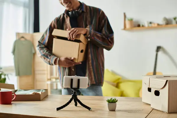 Young African American male blogger arranging boxes while filming with phone camera. — Foto stock