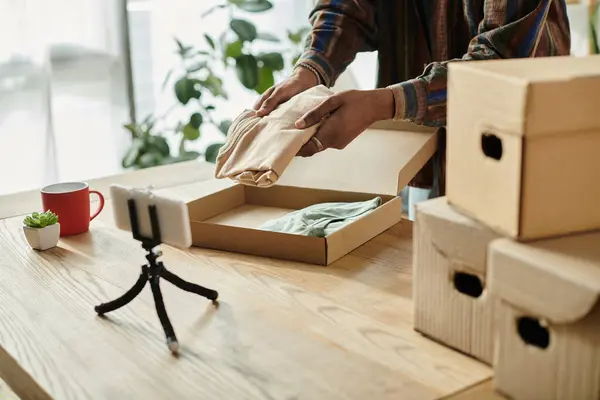 Young African American male blogger talking on phone camera while putting boxes on a table. — Stock Photo