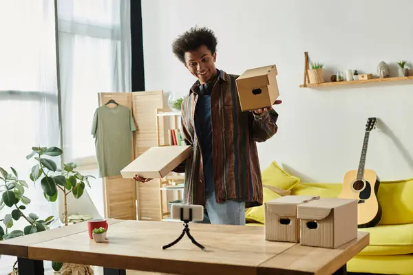 Young African American man holding cardboard box while vlogging in living room. — Fotografia de Stock