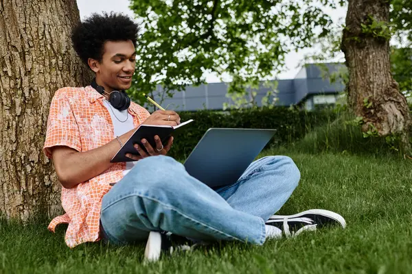 Black man working on laptop in grassy park setting. — Stock Photo