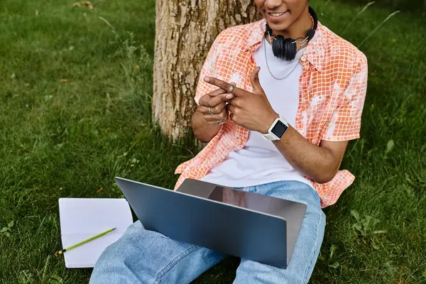 Young man with laptop under tree in park. — Stockfoto
