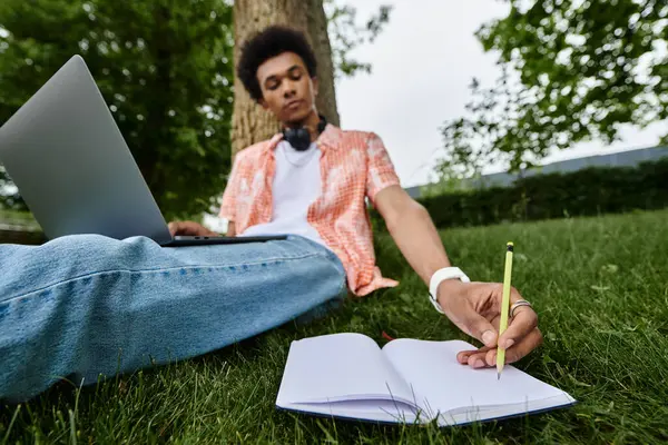 A man sits in grass with laptop and notebook. — Stock Photo