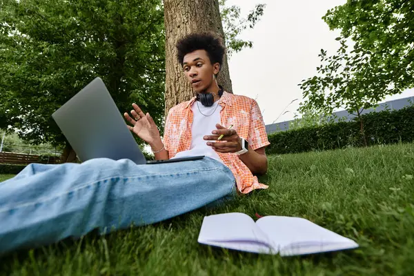 A young man of African American descent sitting peacefully on grass, working on a laptop. — Stock Photo