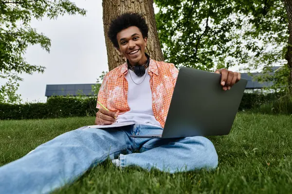 A young African American man sitting on grass with a laptop in a park. — стоковое фото