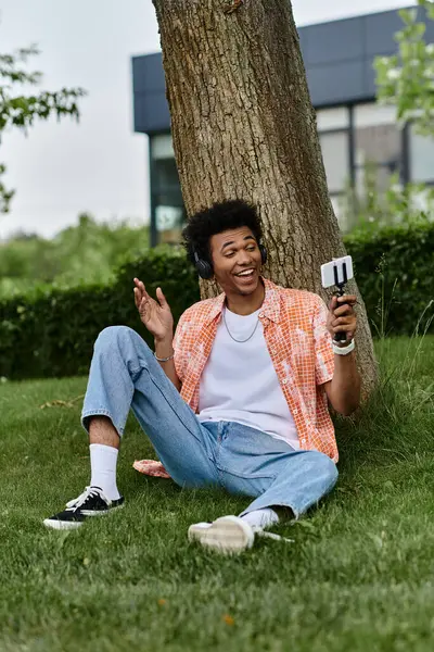 A young man of African descent sits on grass beside a tree. — Fotografia de Stock