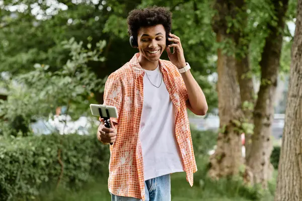 A young man, enjoying a leisurely walk in the park, fixated on his phone. — Stockfoto