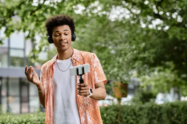 A young african american man enjoys the tranquility of a park while holding a cell phone. — Stock Photo