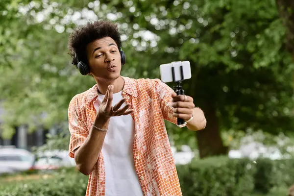 A young African American man capturing a selfie amidst lush greenery in the park. — Stock Photo