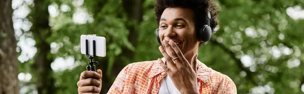 A young African American man in a park taking a selfie with his cell phone. — Stock Photo