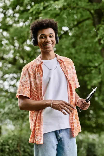Young man in headphones listening to music, standing in a park. — Stock Photo