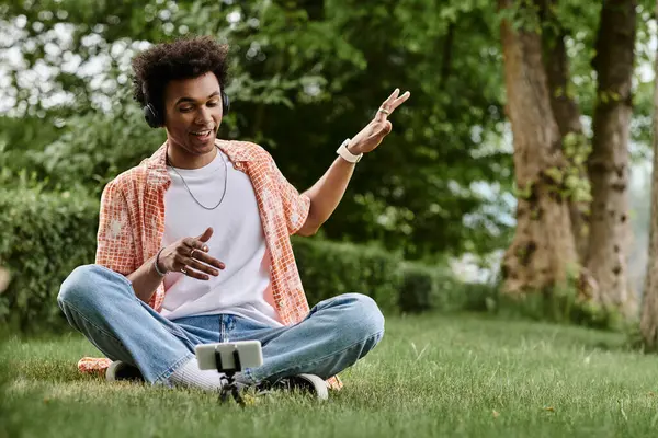 Young man of African descent sitting on grass, energetically pointing at phone. — Stock Photo