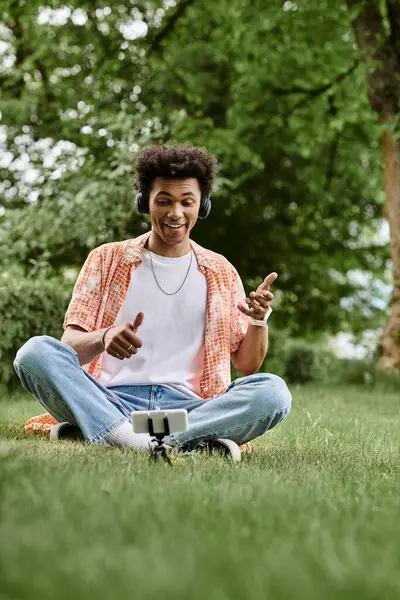 Young African American man sitting on grass, pointing at his phone. — Photo de stock