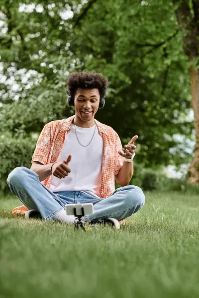 Young African American man sitting on grass, pointing at his phone. — стоковое фото