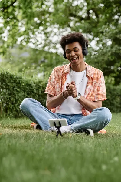 A young man of African American descent sitting on the grass, immersed in music. — Stockfoto