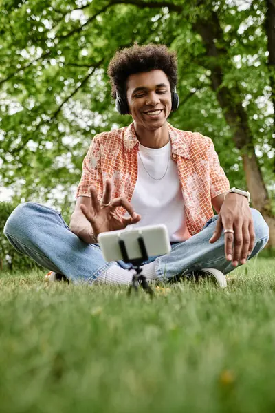 Young man immersed in music sits on grass in park with headphones on. — Stock Photo