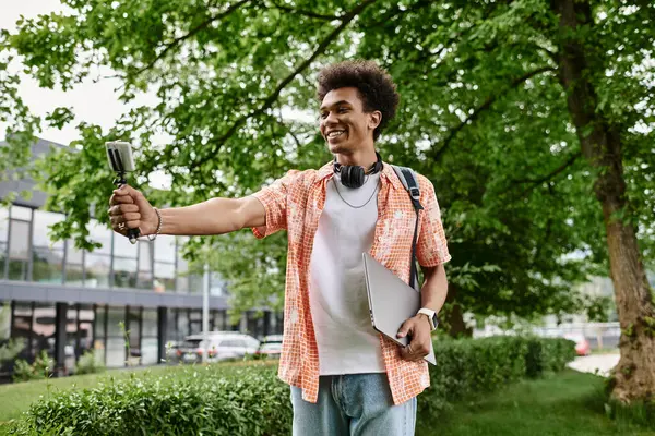 A young African American man smiles while taking a selfie in a park. — стоковое фото