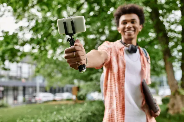 A young man, African American, snapping a selfie in the park with his phone. — Stock Photo
