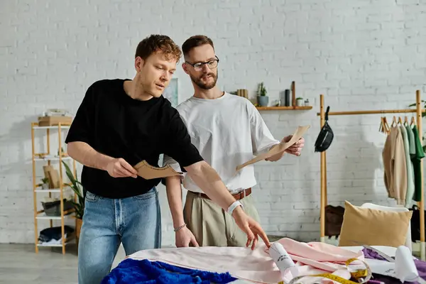 Dos hombres enamorados muestran sus creaciones de diseño frente a la cama de moda. - foto de stock