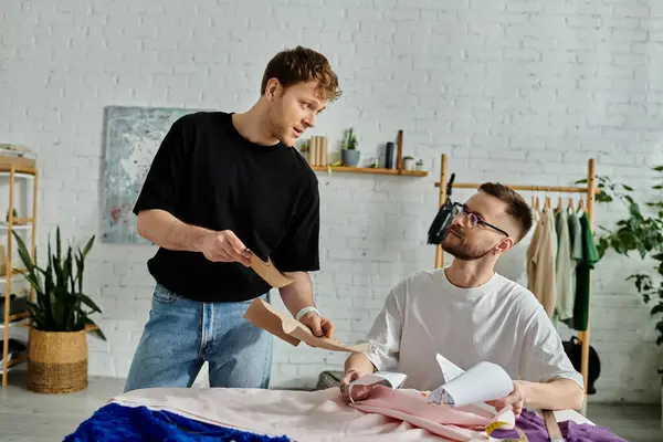 Two men, a gay couple, work together in a designer workshop cutting a piece of paper for their trendy attire. — Stock Photo