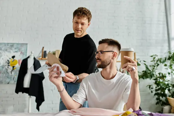 A man sits on a bed as his partner holds a piece of paper in a designer workshop. — Stock Photo
