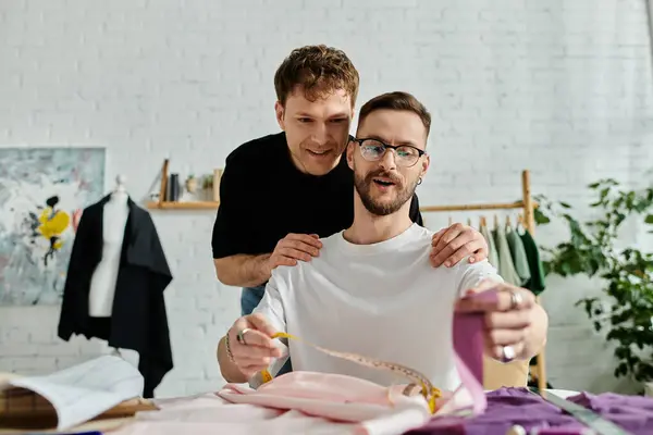 Dos diseñadores examinan una camisa colocada sobre una mesa en su taller de moda. - foto de stock