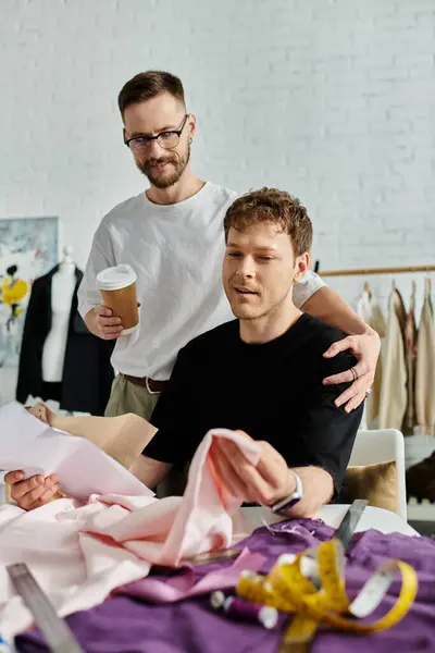 Two men, a gay couple, stand side by side in a designer workshop, collaborating on creating trendy attire. — Stock Photo