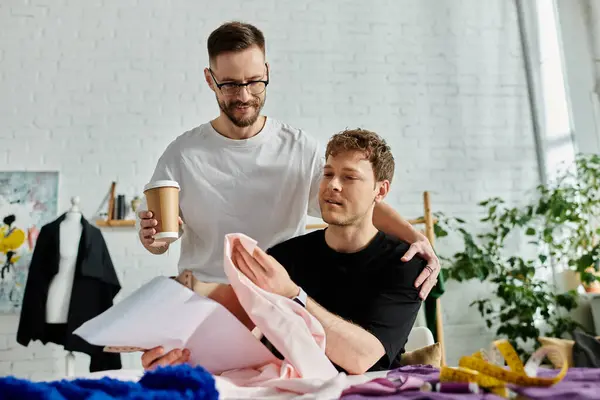 Dos hombres, parte de un elegante dúo de diseño LGBTQ, comparten un momento tranquilo mientras sostienen el café. - foto de stock