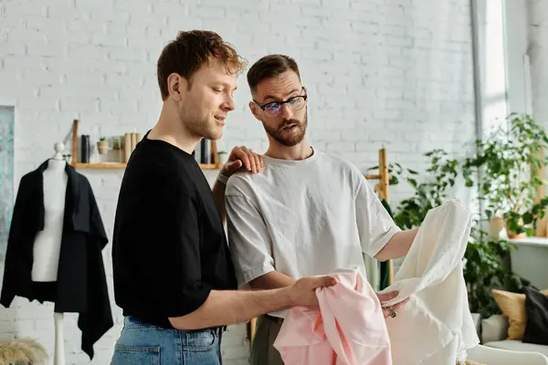 Dois homens, um casal gay, estão lado a lado em uma oficina de designer, colaborando em trajes da moda. — Fotografia de Stock