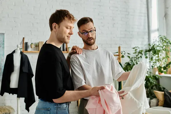 Two men, a gay couple, stand side by side in a designer workshop, collaborating on trendy attire. — Stock Photo