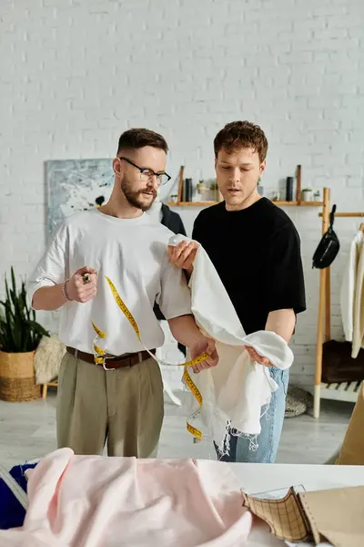 Dois homens colaboram na concepção de trajes de moda em uma oficina elegante. — Fotografia de Stock