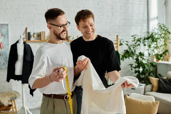 Deux designers, un couple gay amoureux, se tiennent côte à côte dans un atelier branché, discutant d'idées pour leurs dernières créations vestimentaires. — Photo de stock