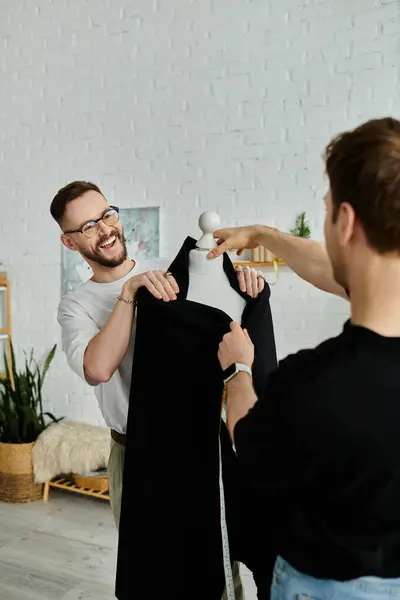 Two men work together in a designer workshop, one holding a black shirt while the other adjusts it. — Stock Photo