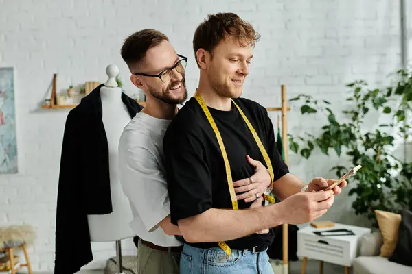 Two men, partners in love and work, standing side by side in a designer workshop, collaborating on trendy attire. — Stock Photo
