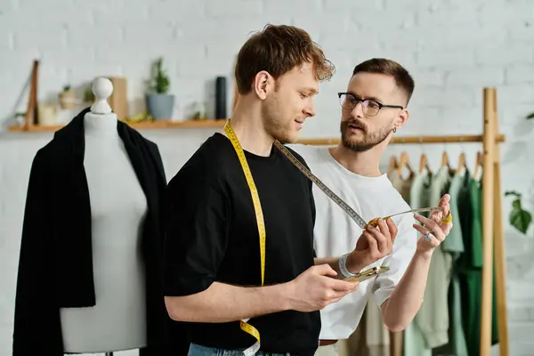 Two men, a gay couple, stand side by side in a designer workshop, focusing on creating trendy attire together. — Stock Photo