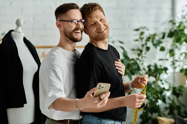 Two men, a gay couple, stand side by side working on trendy attire in their designer workshop. — Stock Photo
