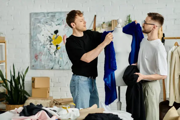 Due uomini, una coppia gay, collaborano alla progettazione di abbigliamento alla moda nel loro laboratorio di design. — Foto stock