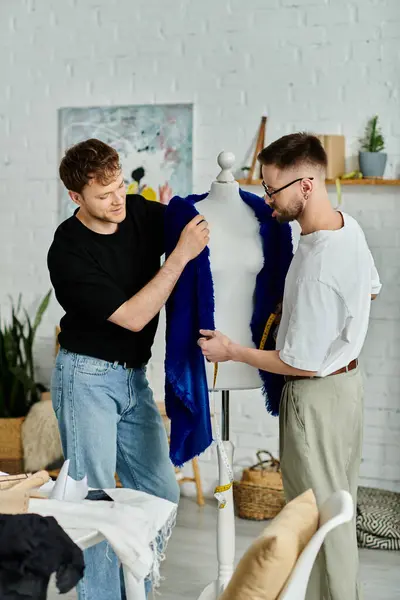Двоє чоловіків оглядають стильну блакитну сорочку, виставлену на манекені в дизайнерській майстерні. — стокове фото