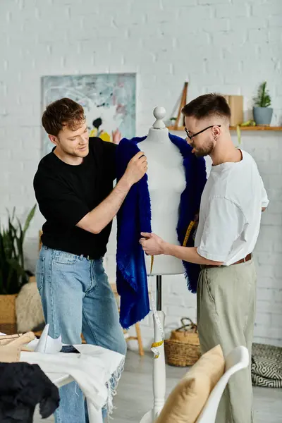 Dos hombres examinan una camisa azul elegante exhibida en un maniquí en un taller de diseño. - foto de stock