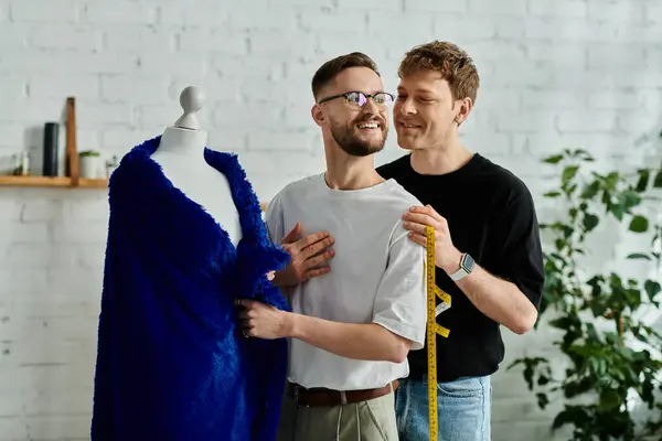 Dos diseñadores masculinos de pie junto a un vestido en un maniquí en un taller creativo. - foto de stock