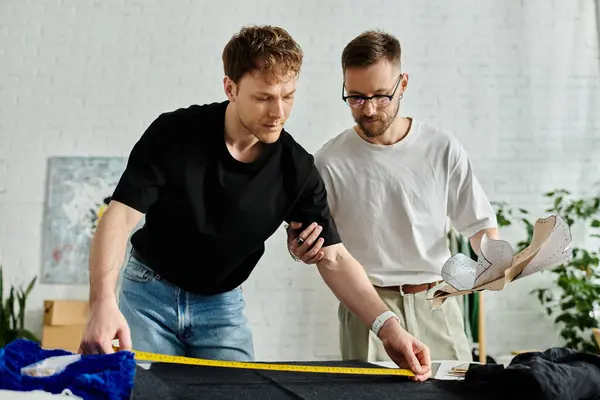 Two men stand side by side in a designer workshop, collaborating on creating trendy attire. — Stock Photo