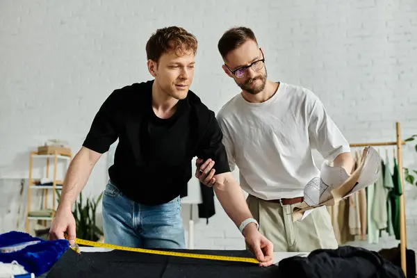 Dos hombres, socios en el diseño y en el amor, de pie lado a lado en su taller de moda. - foto de stock