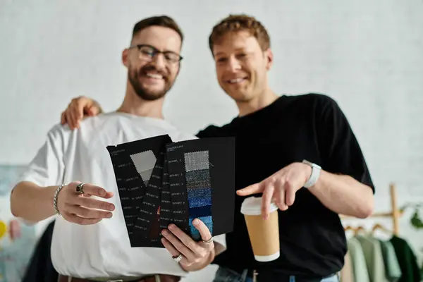 Two men, a gay couple in love, stand side by side in a designer workshop, working together on creating trendy attire. — Stock Photo