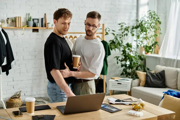 Dos hombres, una pareja gay, están en el taller, absortos en la pantalla de su portátil. - foto de stock