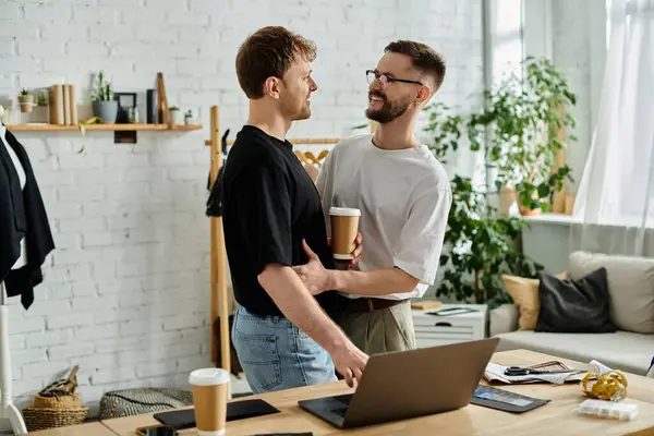 Two designers, a gay couple, stand in front of a laptop, collaborating on trendy attire in their workshop. — Stock Photo