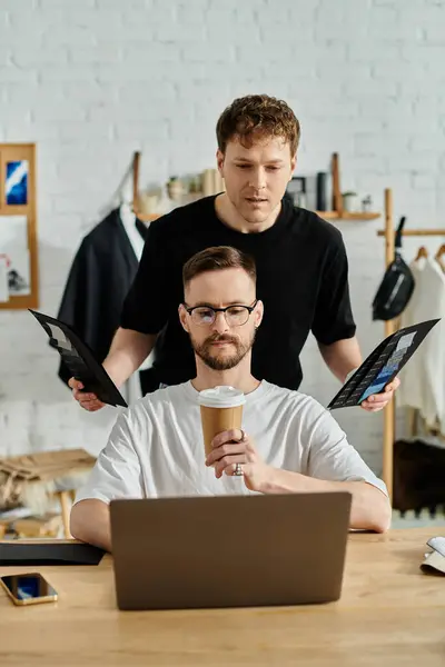 A man sits at a table, engrossed in his laptop, while working on designing trendy attire for his fashion workshop. — Stock Photo