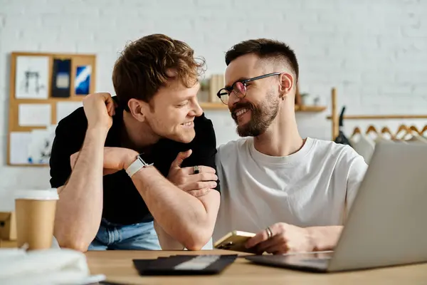 Two men, a gay couple, sit at a table together, focused on a laptop screen in a designer workshop. — Stock Photo