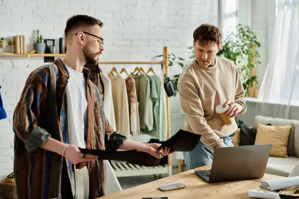 Two men in designer workshop collaborating on laptop, crafting trendy attire. — Stock Photo